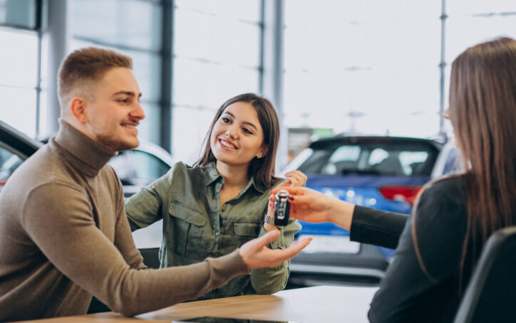 Young couple talking to a sales person in a car showroom