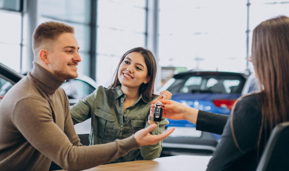 Young couple talking to a sales person in a car showroom